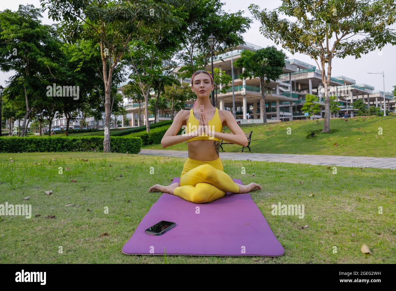 Exercice de yoga - femme faisant du yoga poser la méditation dans le sport de parc public, concept sain. Vêtements de sport jaunes Banque D'Images
