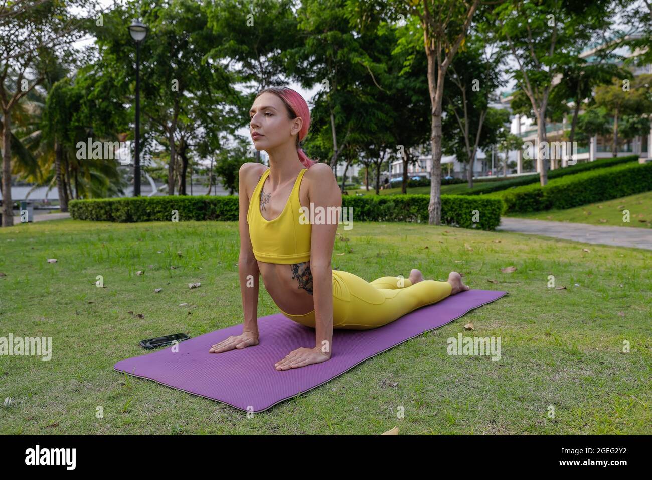 FIT Girl faisant yoga stretching yoga en ligne dans le parc. Divertissement et éducation sur l'Internet. Vêtements de sport jaunes Banque D'Images