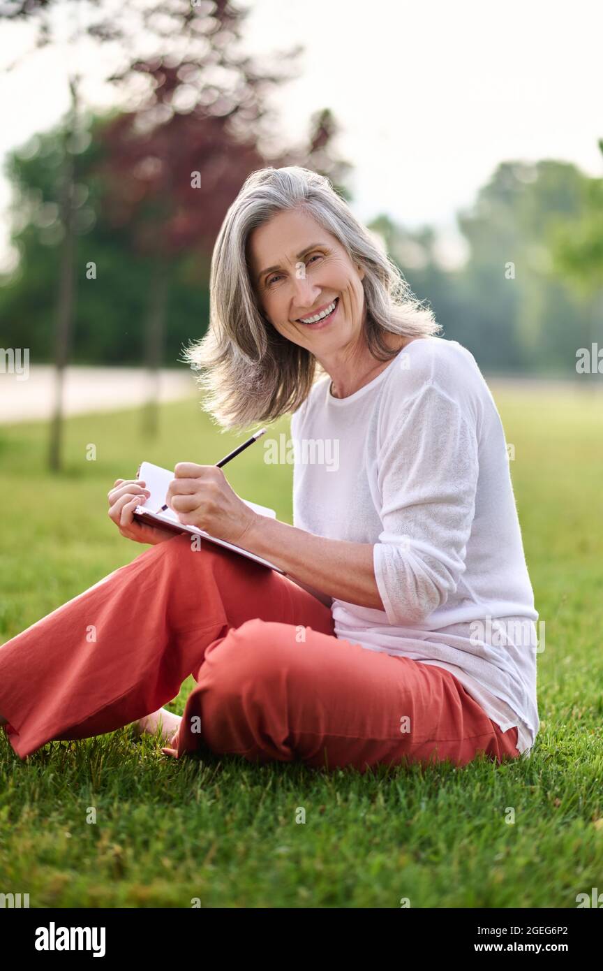 Femme souriante prenant des notes sur la pelouse Banque D'Images