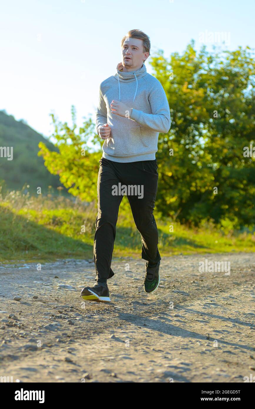 Homme courant jogging dans la nature rurale à la belle journée d'été. Modèle de fitness sportif entraînement ethnique caucasien en extérieur. Banque D'Images