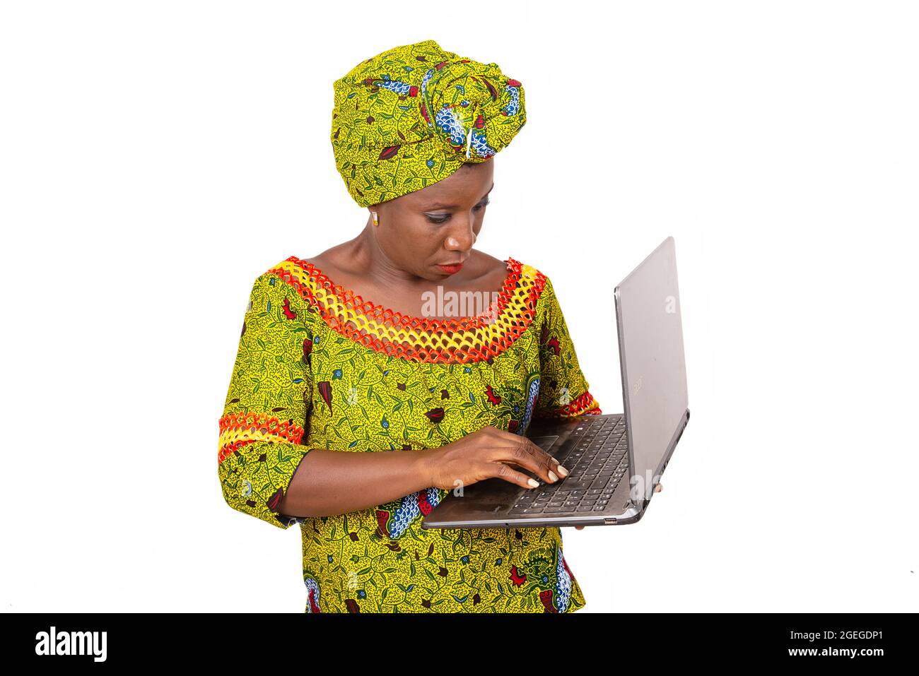 belle femme adulte africaine vêtue de tissu de longe et de foulard vert est debout tout en manipulant un ordinateur portable dans la main tout en souriant Banque D'Images