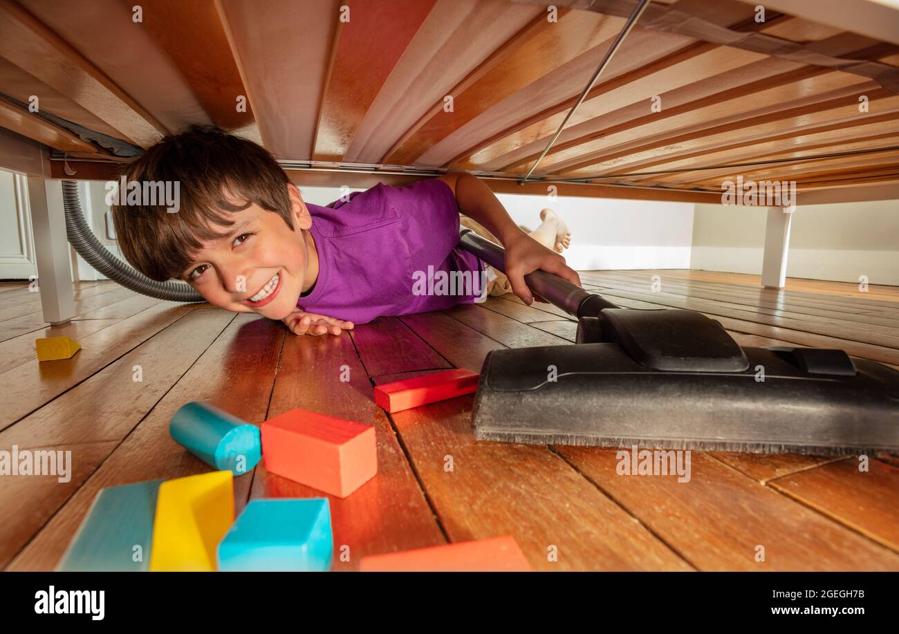 Garçon sous le lit nettoyer le sol avec un aspirateur Banque D'Images