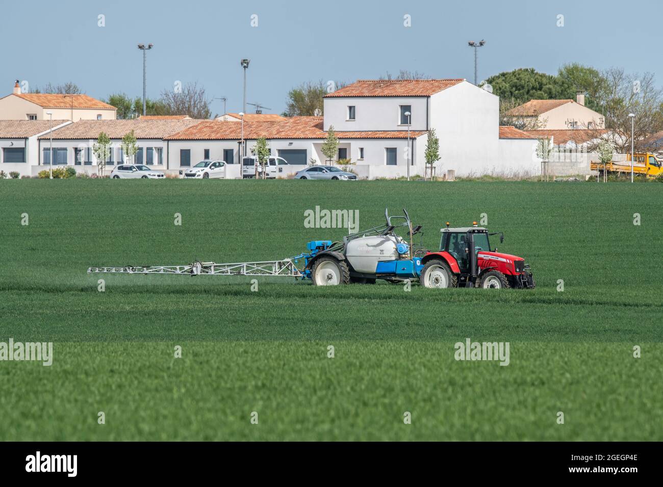 Agriculteur pulvérisant des pesticides sur un champ de blé près d'une propriété immobilière à Saint Rogatien (sud-ouest de la France) Banque D'Images
