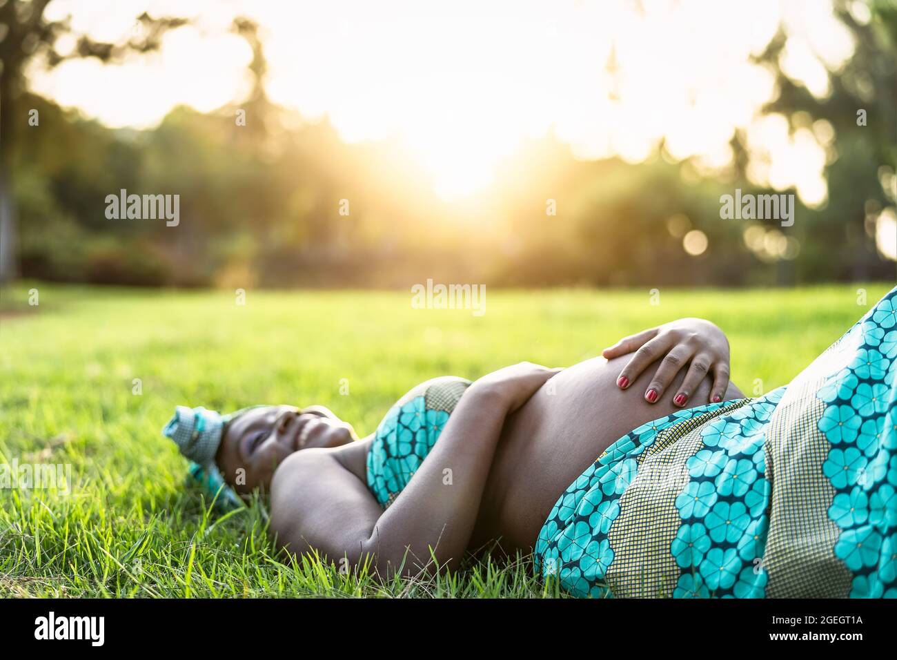Jeune femme enceinte africaine allongé sur un parc d'herbe verte pendant le coucher du soleil - concept de mode de vie de maternité Banque D'Images