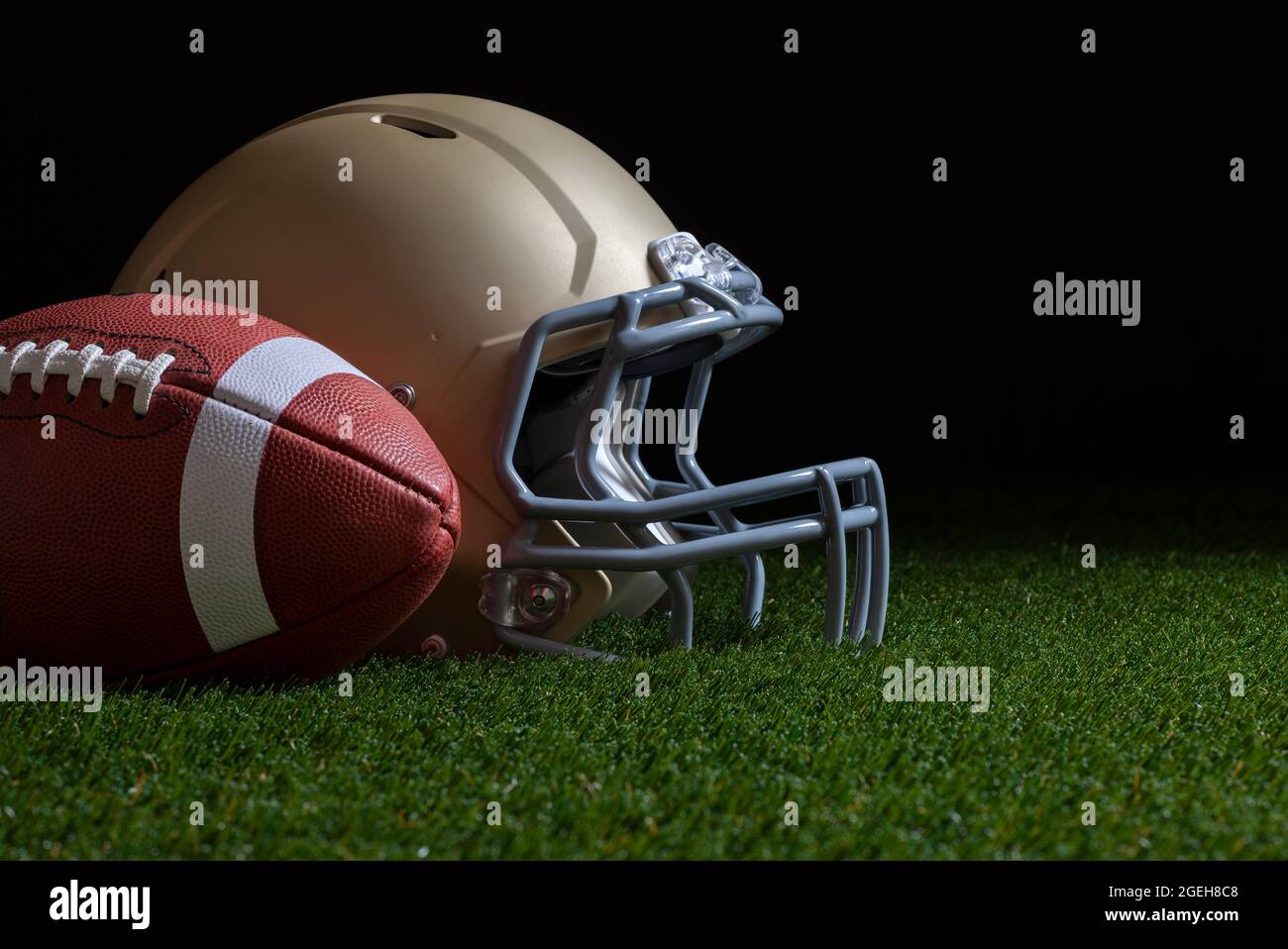 Vue basse du ballon de football et du casque doré sur l'herbe avec fond sombre Banque D'Images