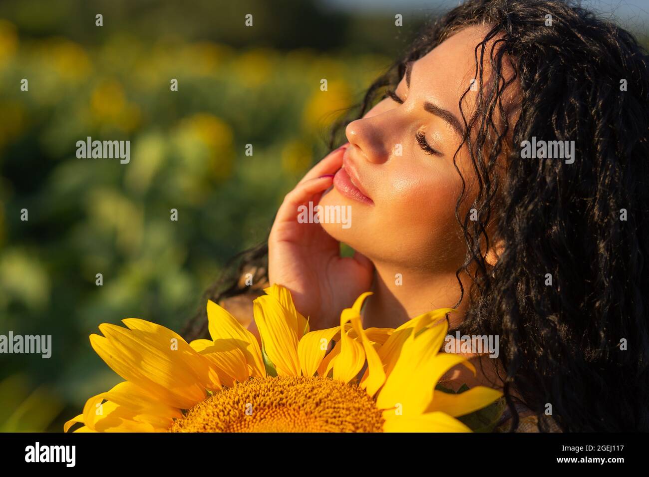 Portrait rapproché d'une jeune femme qui regarde derrière un grand tournesol. Concept d'été. Banque D'Images