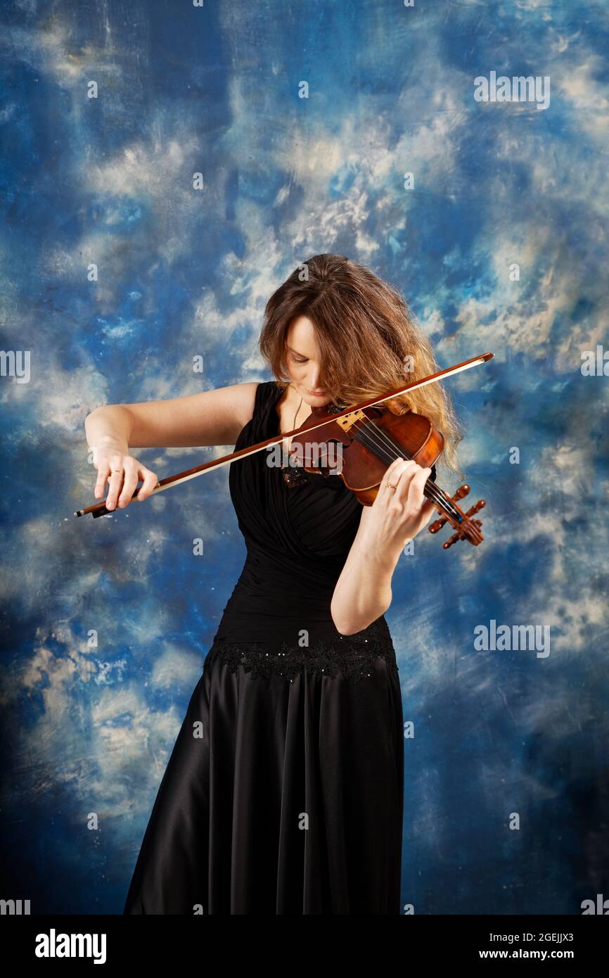 Jeune femme jouant le violon sur fond bleu abstrait. Banque D'Images