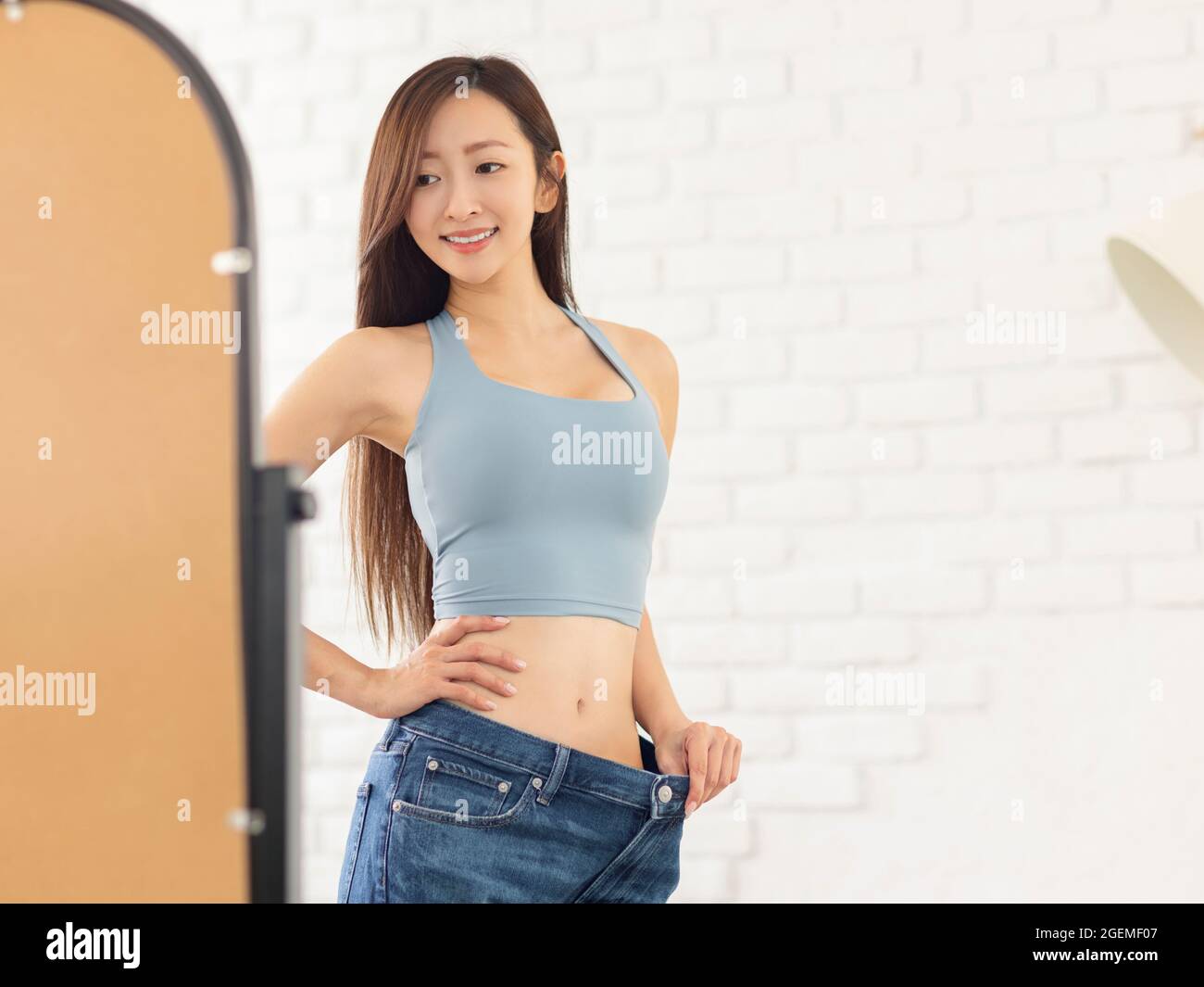 Jeune femme en jeans grande taille et debout devant le miroir. Concept de perte de poids Banque D'Images