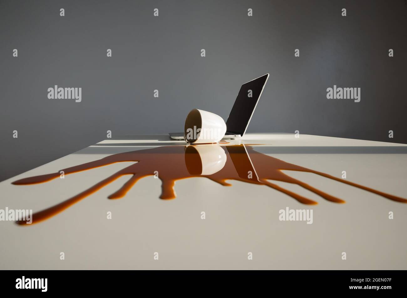 Une tasse de café noir a été renversé sur un ordinateur portable, sur un bureau blanc. Banque D'Images Une tasse de café noir a été renversé sur un ordinateur portable, sur un bureau blanc. Banque D'Images