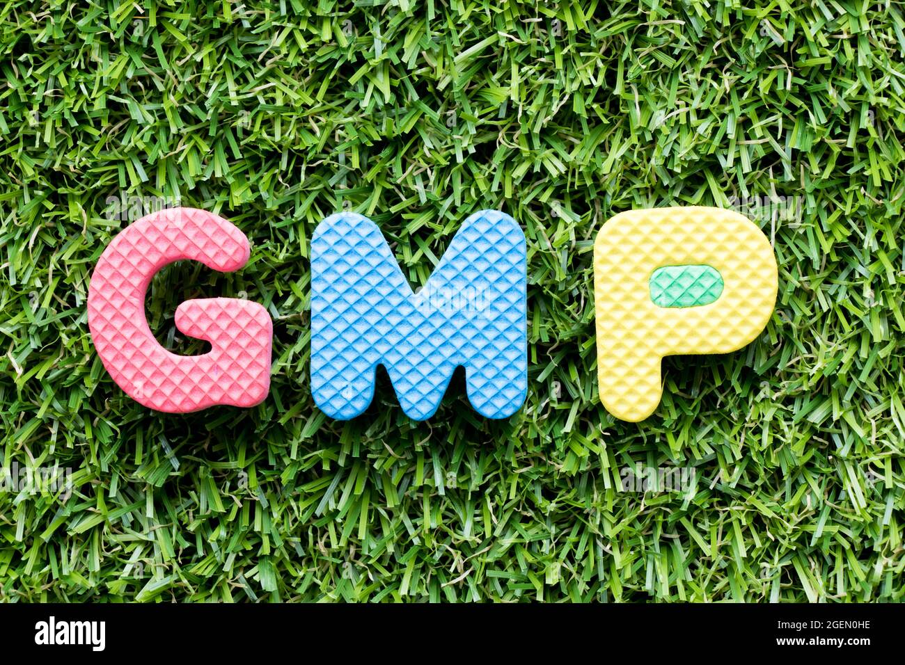 Lettre de couleur en mot GMP (abréviation de bonnes pratiques de fabrication) sur fond d'herbe verte artificielle Banque D'Images