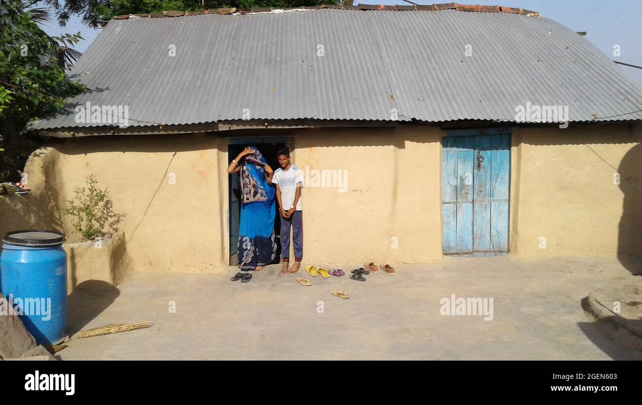 La femme rurale indienne et son garçon debout à l'entrée de leur maison regardent la caméra. Banque D'Images