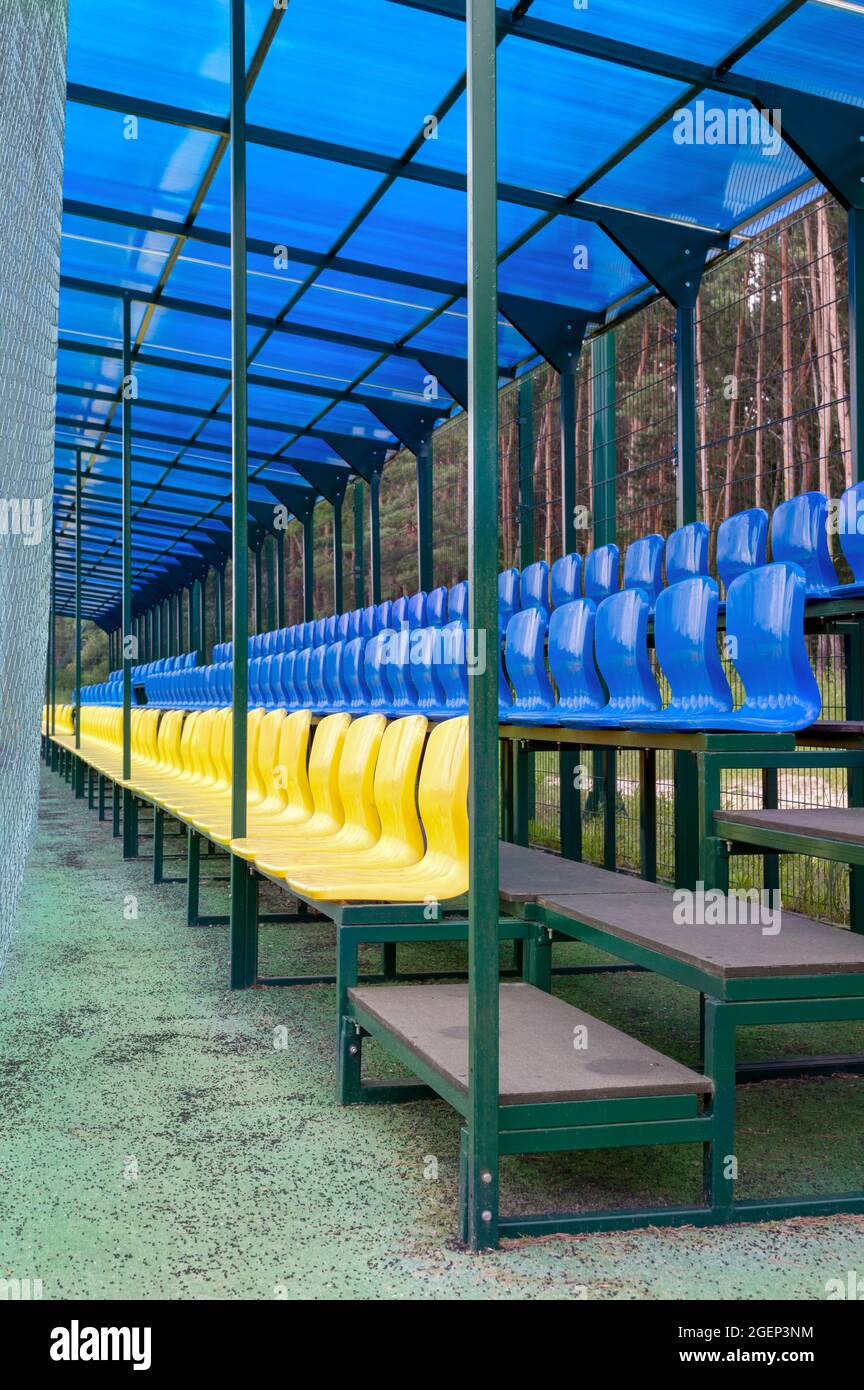 Petit tribune avec des sièges jaunes et bleus pour les spectateurs avec un toit, un filet de protection au stade de la ville. Banque D'Images