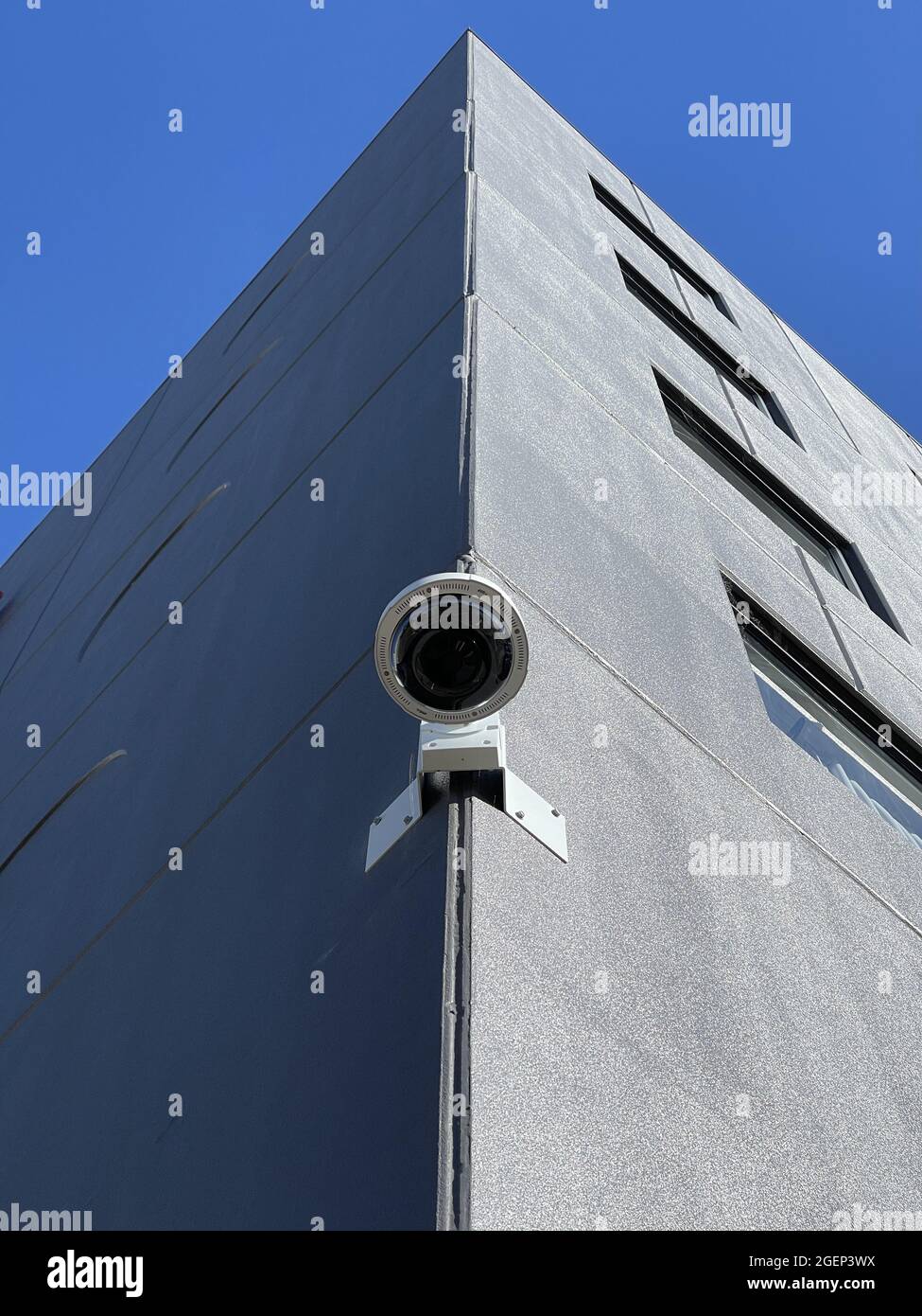 Gros plan d'une caméra de surveillance montée sur le bord d'un bâtiment contre un ciel bleu Banque D'Images