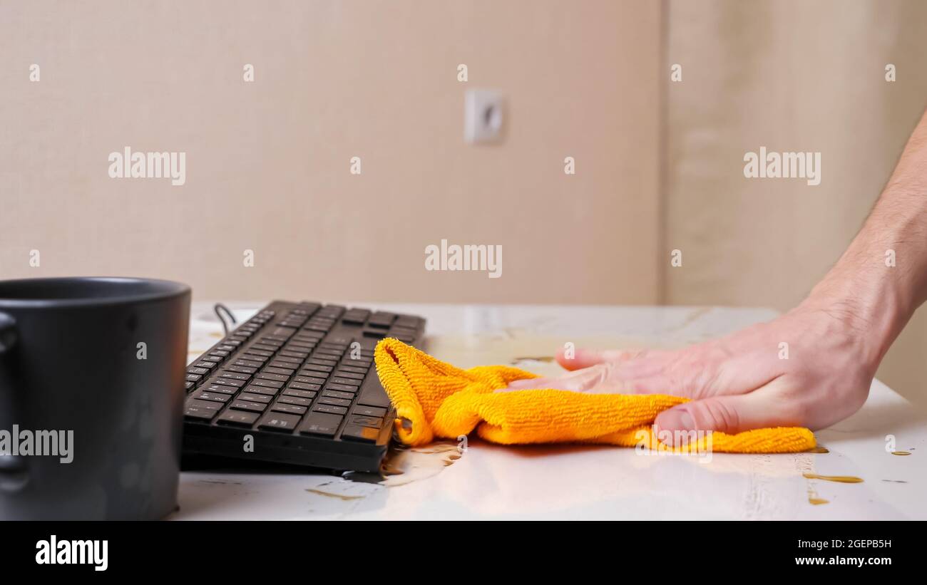 La main de l'homme nettoie le café renversé de la table et du clavier Banque D'Images La main de l'homme nettoie le café renversé de la table et du clavier Banque D'Images