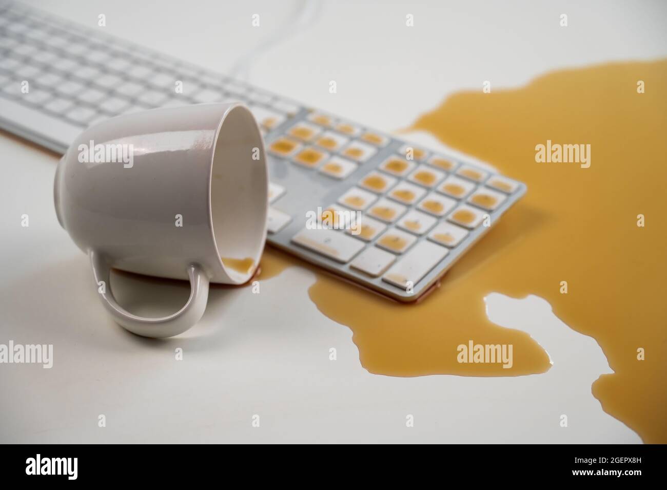 Tasse de café noir renversée sur le clavier de l'ordinateur sur la table blanche. Banque D'Images Tasse de café noir renversée sur le clavier de l'ordinateur sur la table blanche. Banque D'Images