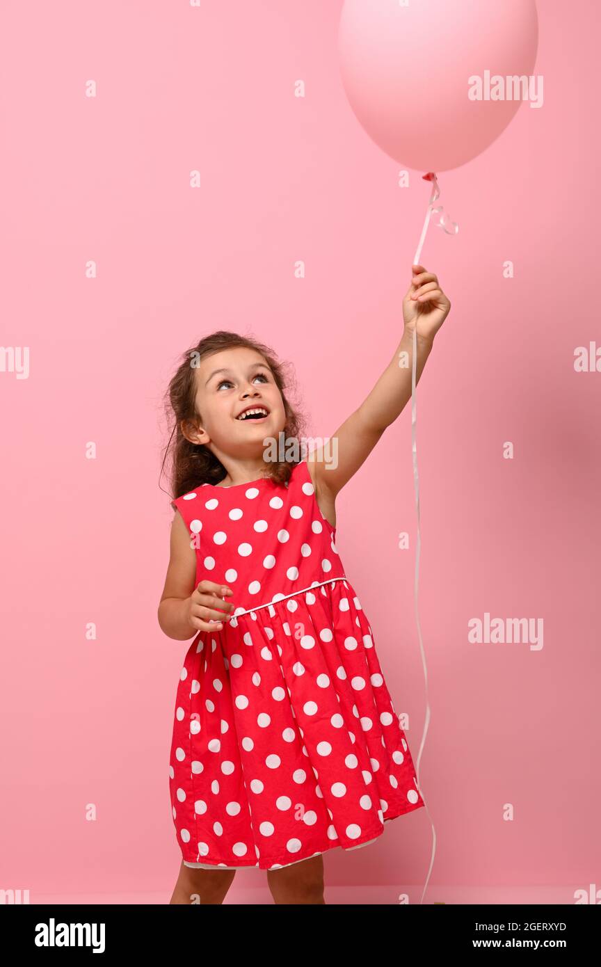 Adorable Magnifique 4 Ans Jolie Fille D Anniversaire En Robe A Pois Rose Tient Deux Ballons Multicolores Se Rejouit De Regarder Un Ballon Vert Dans Son Han Photo Stock Alamy