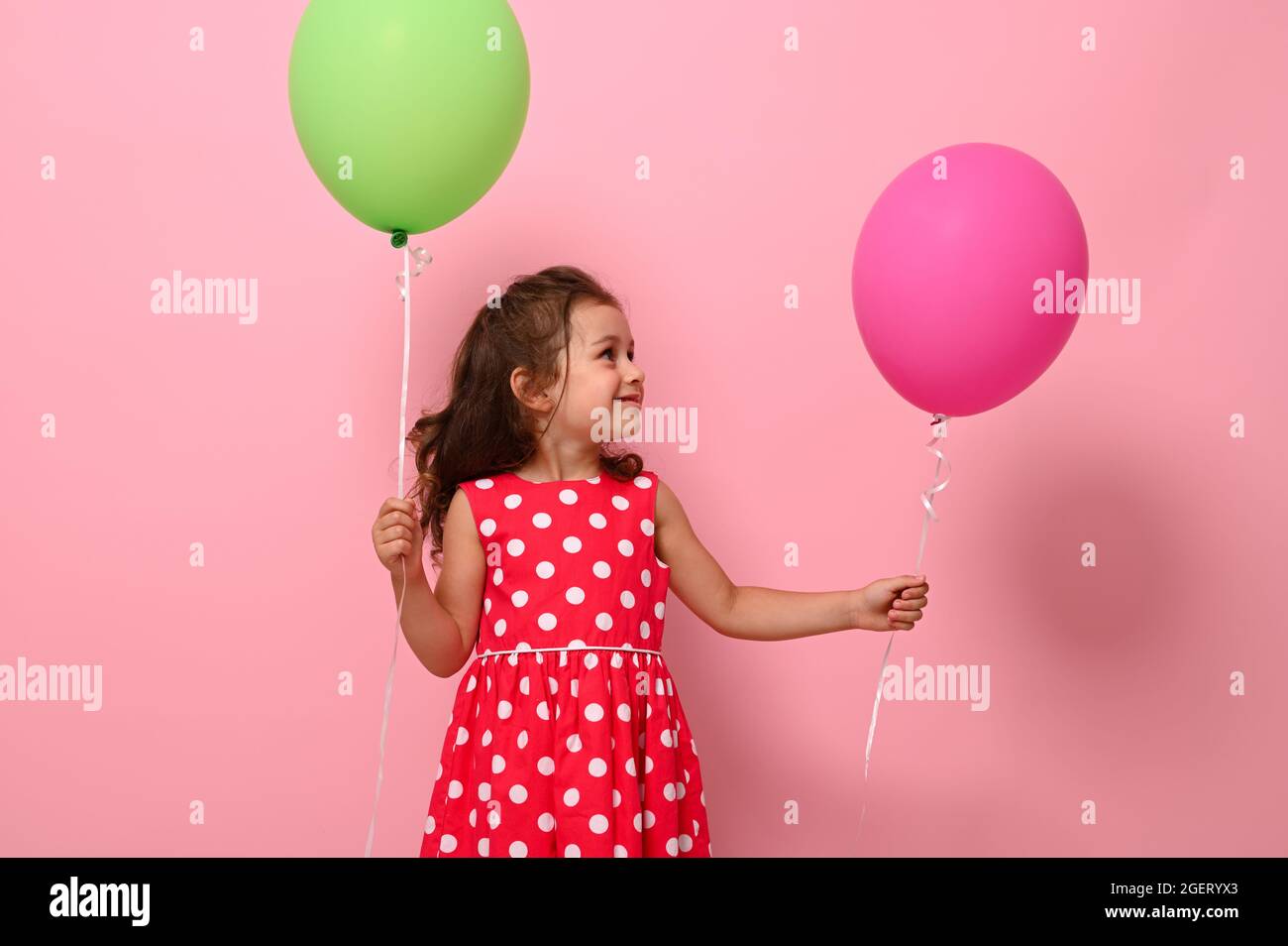Adorable Magnifique 4 Ans Jolie Fille D Anniversaire En Robe A Pois Rose Tient Deux Ballons Multicolores Se Rejouit De Regarder Un Ballon Vert Dans Son Han Photo Stock Alamy