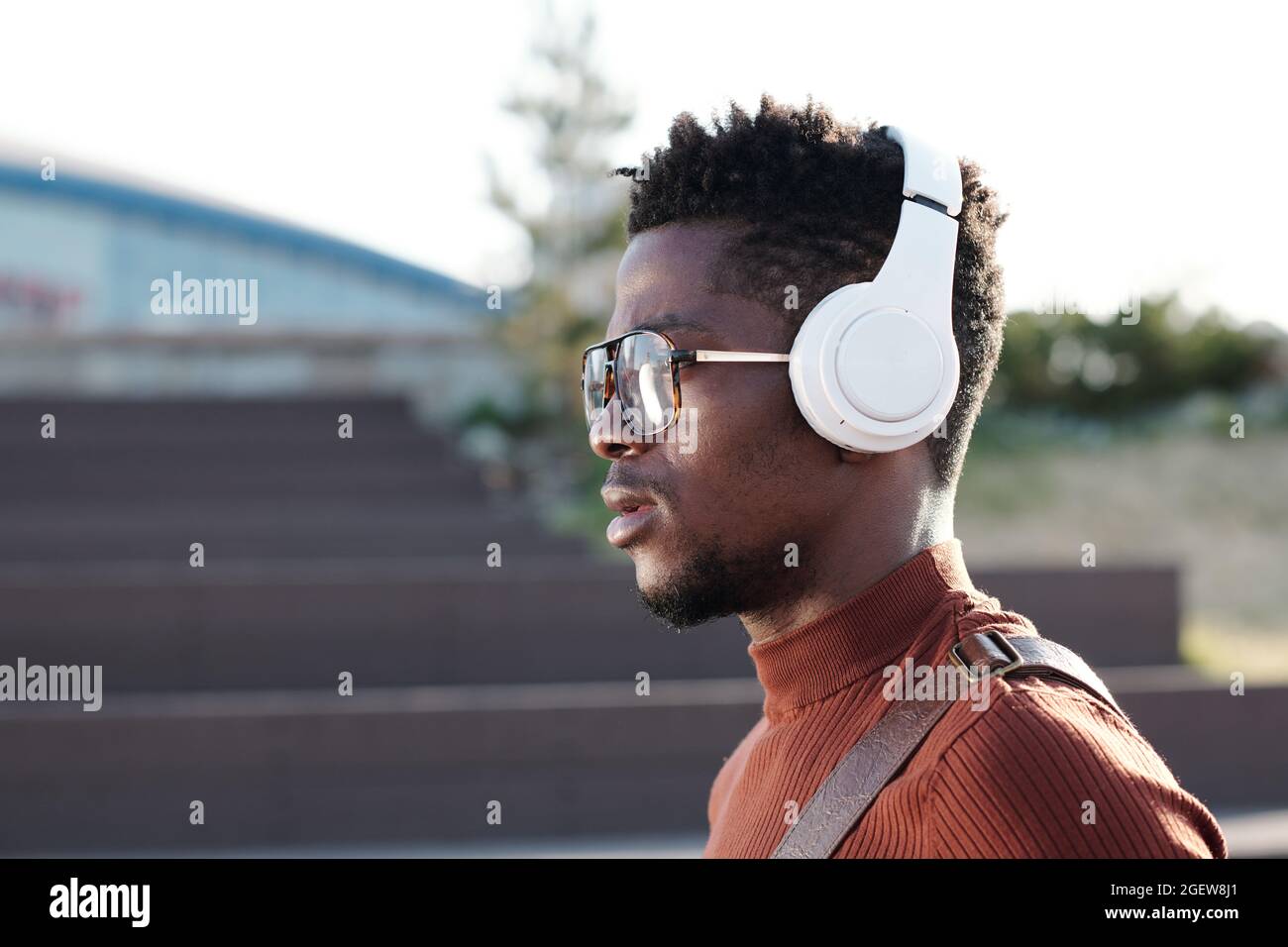 Jeune homme sérieux d'origine africaine écoutant de la musique dans des écouteurs en milieu urbain Banque D'Images