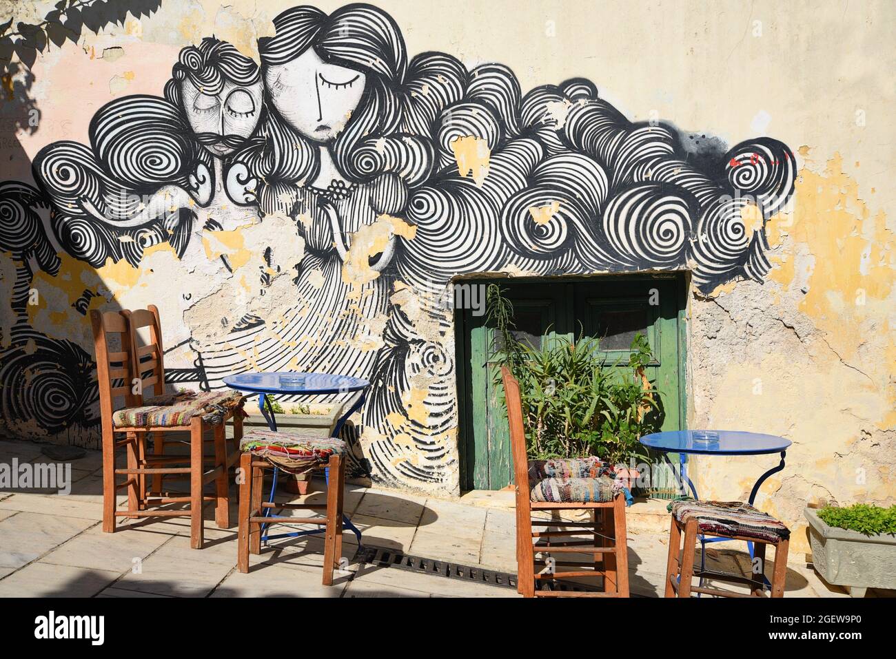 Vue panoramique d'un café local patio avec un mur de graffiti abîmé et délavé en arrière-plan, Anafiotika Athènes Grèce. Banque D'Images