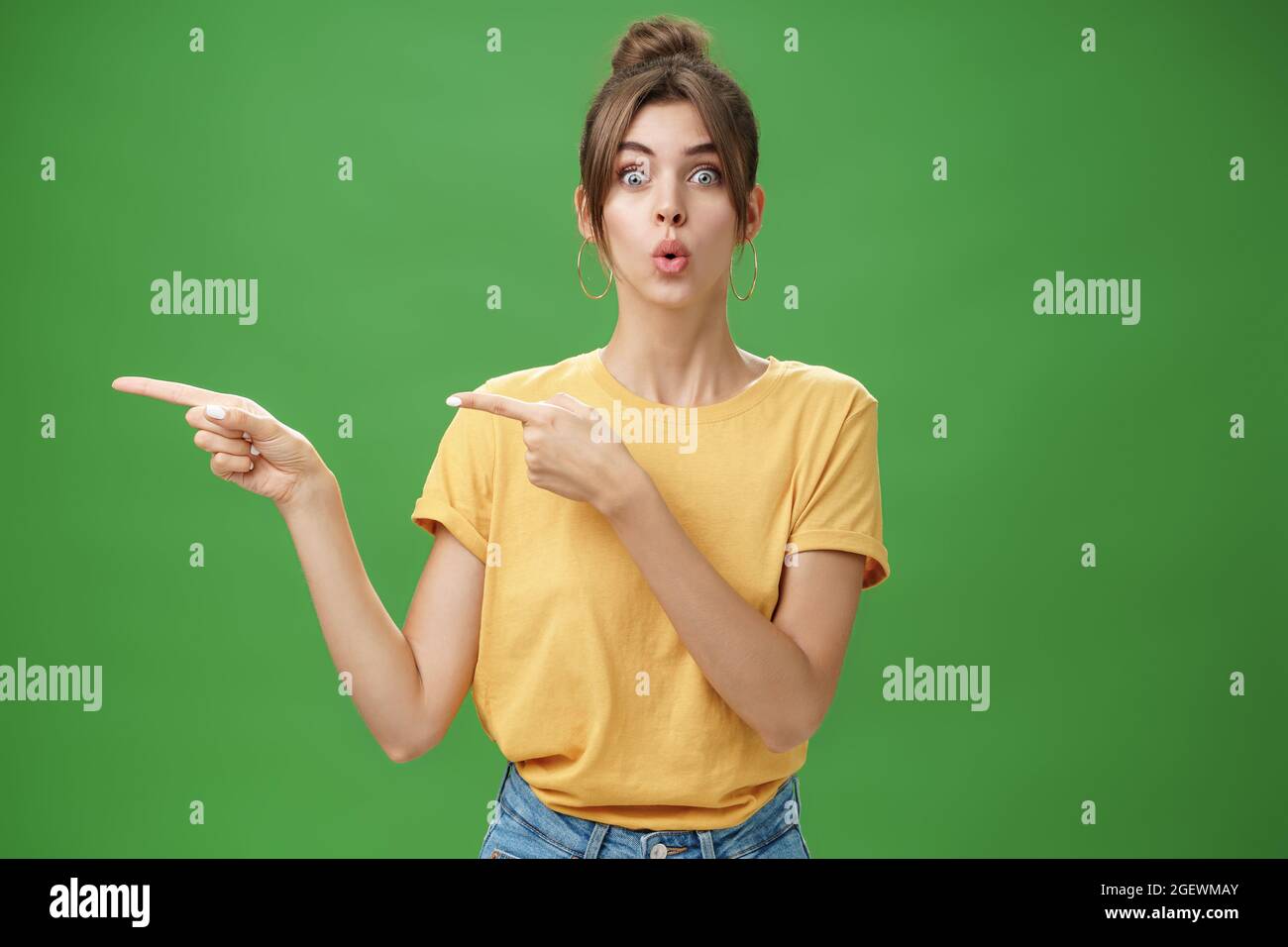 Femme réagissant à des ventes impressionnantes dans le magasin proche pointant à gauche et en regardant impressionné et excité les lèvres pliantes de l'appareil photo désir et étonnement regarder Banque D'Images