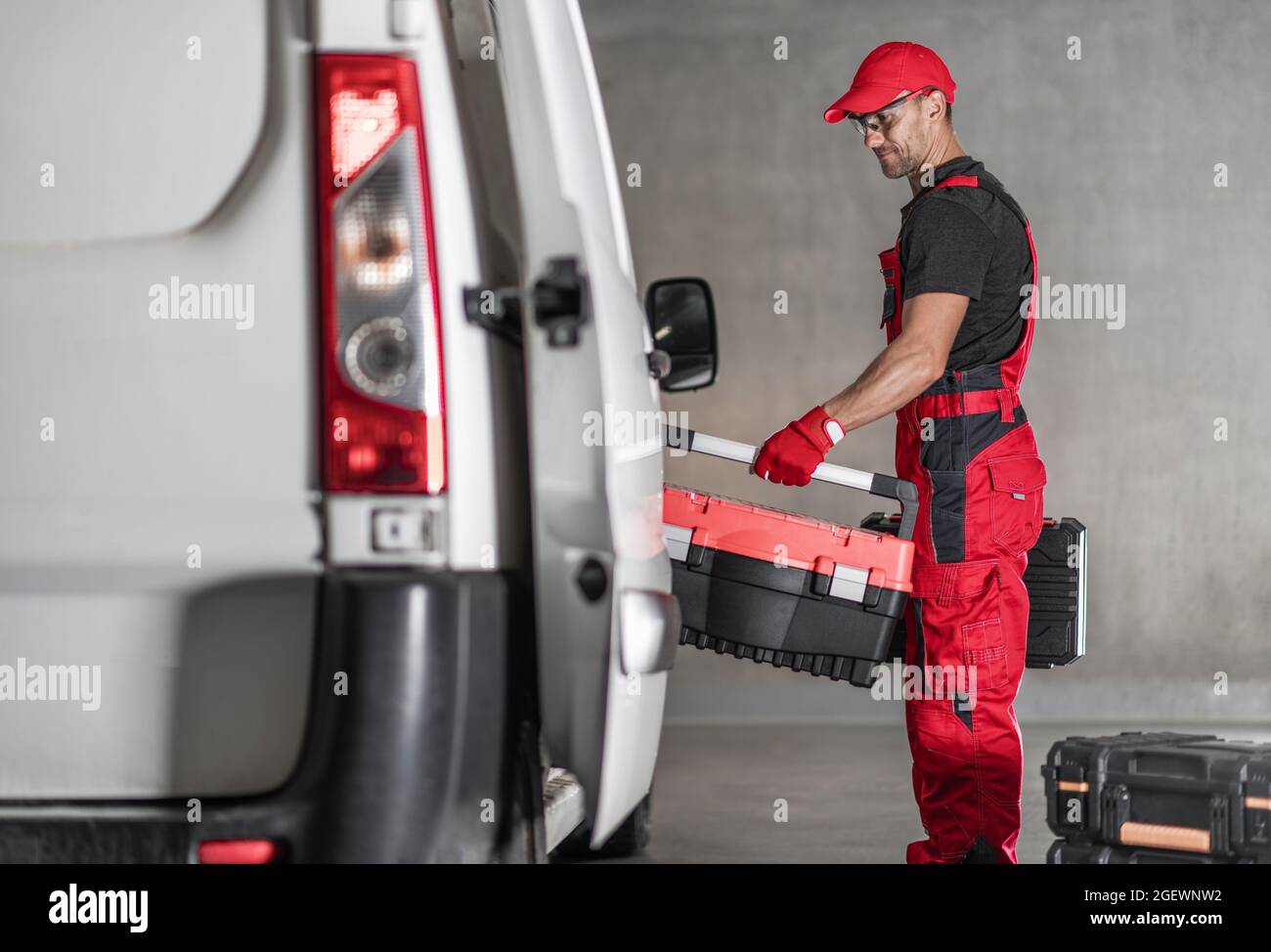 Souriant travailleur d'entrepreneur caucasien dans ses années 40 chargement de ses boîtes à outils dans sa camionnette commerciale. Thème véhicules commerciaux. Banque D'Images Souriant travailleur d'entrepreneur caucasien dans ses années 40 chargement de ses boîtes à outils dans sa camionnette commerciale. Thème véhicules commerciaux. Banque D'Images