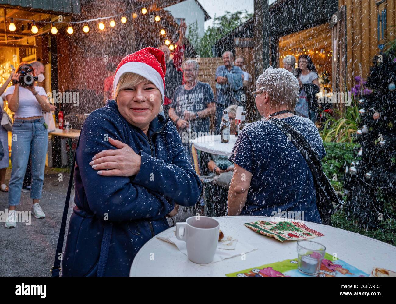 Nachrodt Wiblingwerde, Allemagne. 21 août 2021. Astrid Pietrzak de Meinerzhagen porte un chapeau de père Noël sur le marché de Noël. Devant un café, les opérateurs laissent la neige artificielle Gundermann s'enlayer, à de nombreux stands, des bougies, des couronnes ou des boules de Noël sont vendues. Ce n'est pas la première fois que le marché de Noël d'été est organisé, mais l'année dernière, il a été victime de la pandémie de Corona. Credit: Markus Klümper/dpa/Alay Live News Banque D'Images