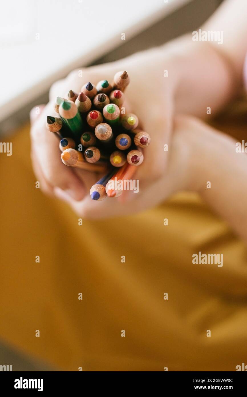 un tas de crayons de couleur dans les mains de la femme sur fond jaune, retour à l'école concept Banque D'Images