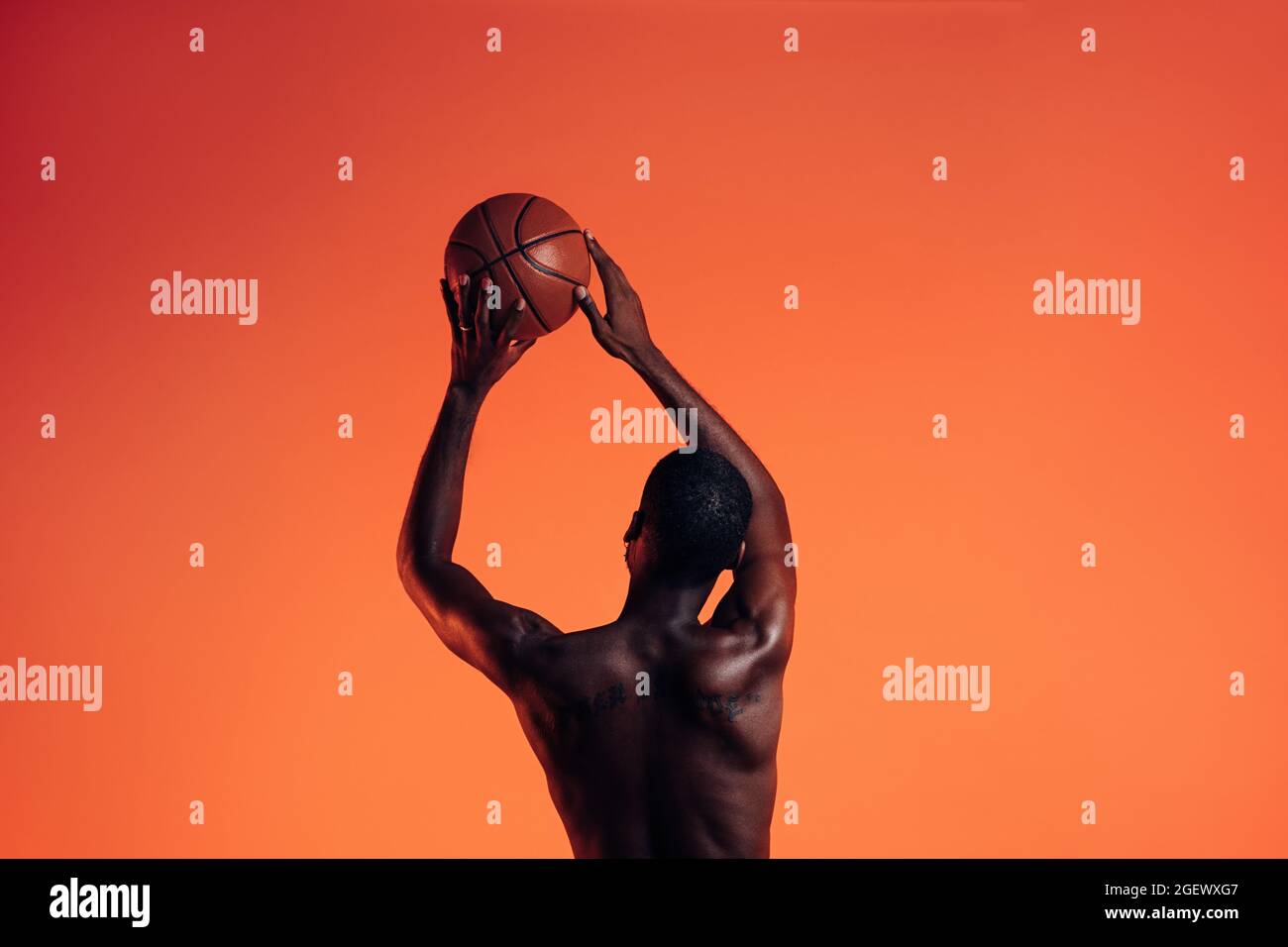 Vue arrière du joueur de basket-ball sur fond orange. Jeune homme en studio se préparant à lancer la balle de panier. Banque D'Images