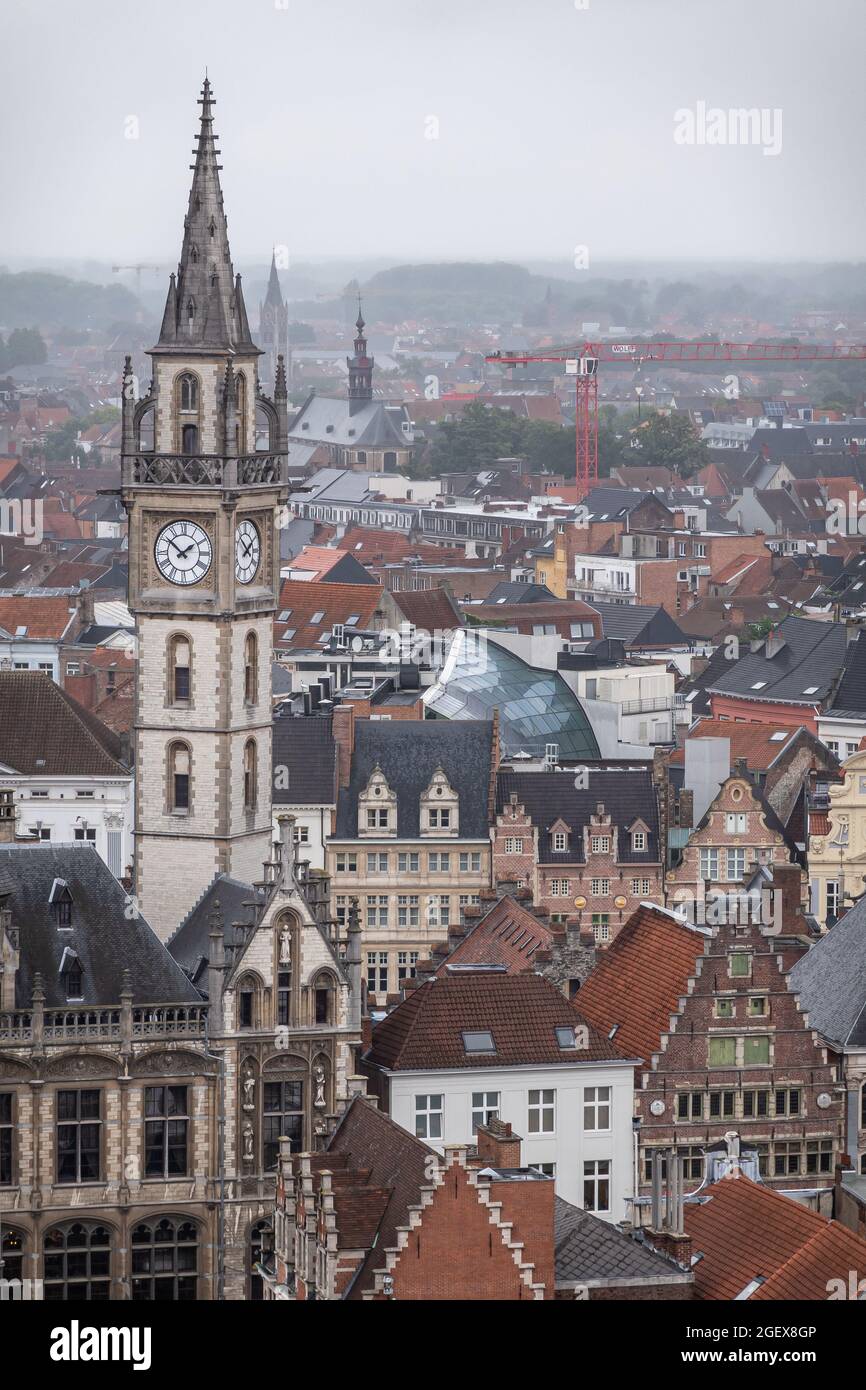 Gand, Flandre, Belgique - 30 juillet 2021 : tour d'horloge postale fine sur un paysage urbain dense sous la pluie avec une grue rouge et des collines vertes à l'arrière. Abun Banque D'Images