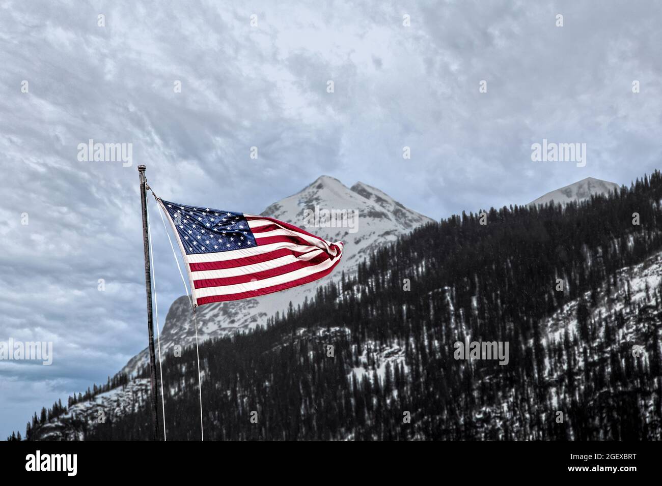 Drapeau américain agitant contre une montagne escarpée avec de la neige sous un ciel couvert. Banque D'Images