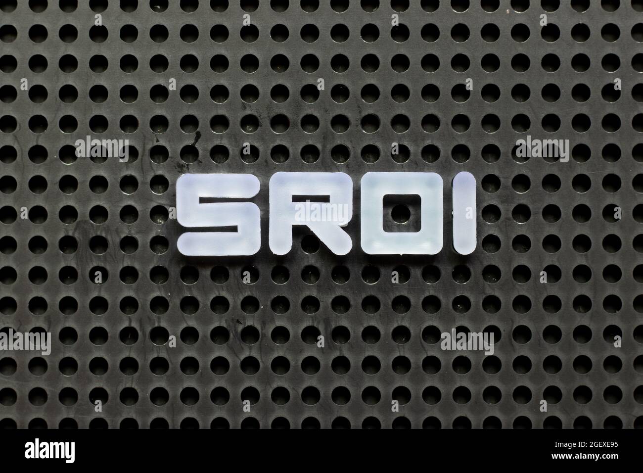 Lettre de couleur blanche dans le mot SROI (abréviation du retour sur investissement social) sur fond perforé noir Banque D'Images