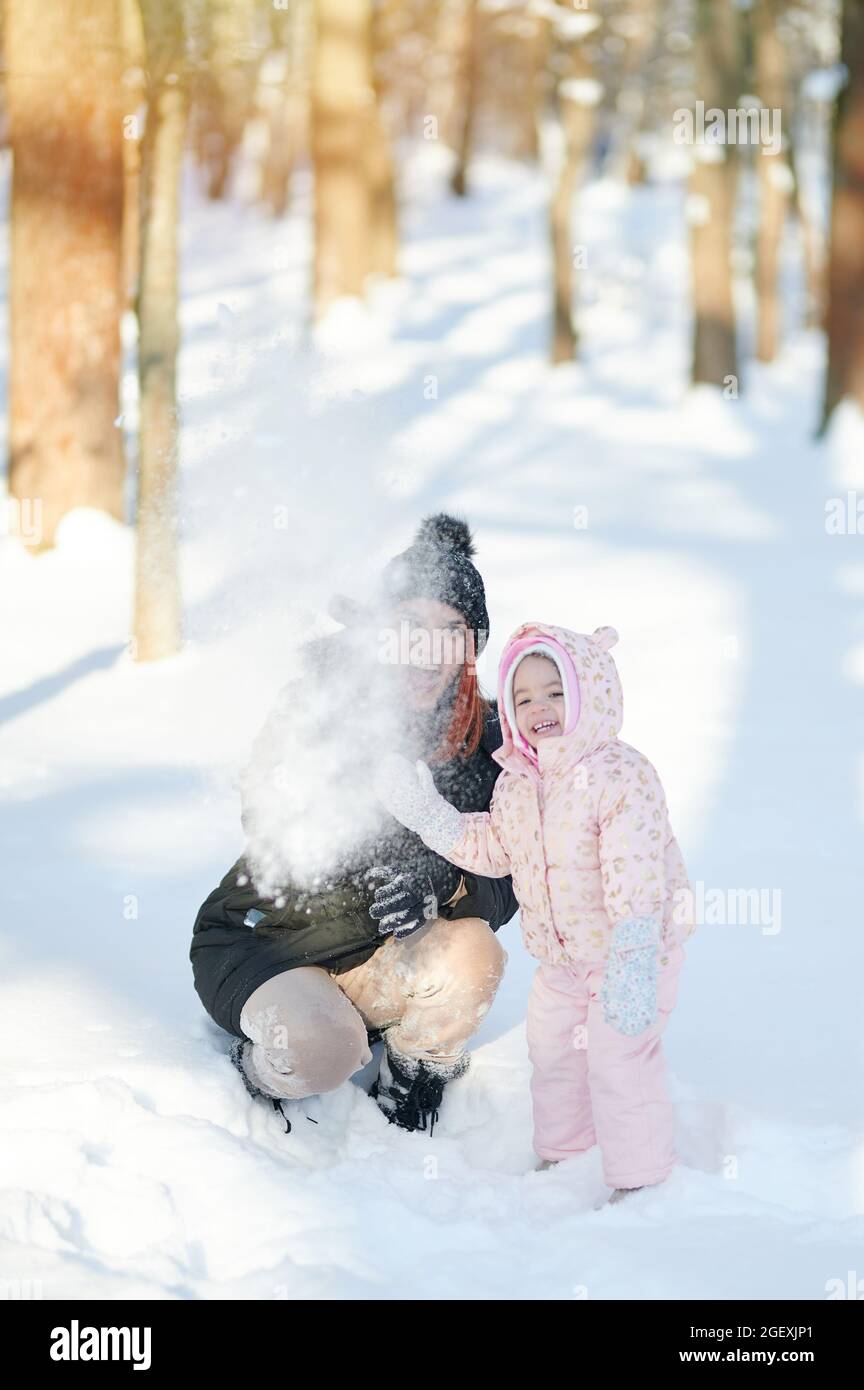 Lancer une maman de neige avec un enfant sur fond ensoleillé de parc d'hiver Banque D'Images