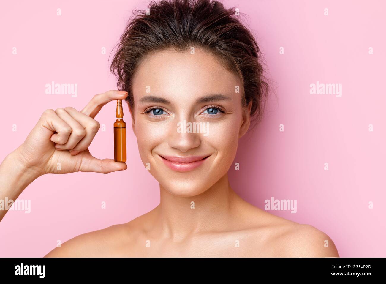 La femme tient une ampoule avec du sérum pour les soins des cheveux ou de la peau. Photo d'une femme attrayante avec un maquillage parfait sur fond rose. Concept de beauté Banque D'Images
