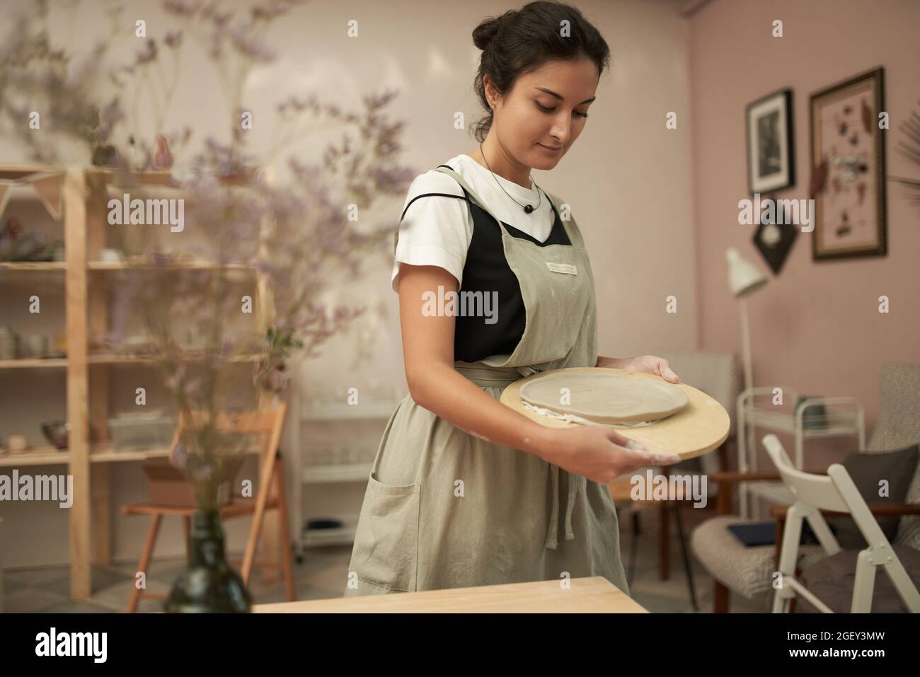 Plateau de transport de jeune céramiste femelle avec plaque d'argile inachevée tout en créant des produits d'artisanat dans un atelier de poterie Banque D'Images