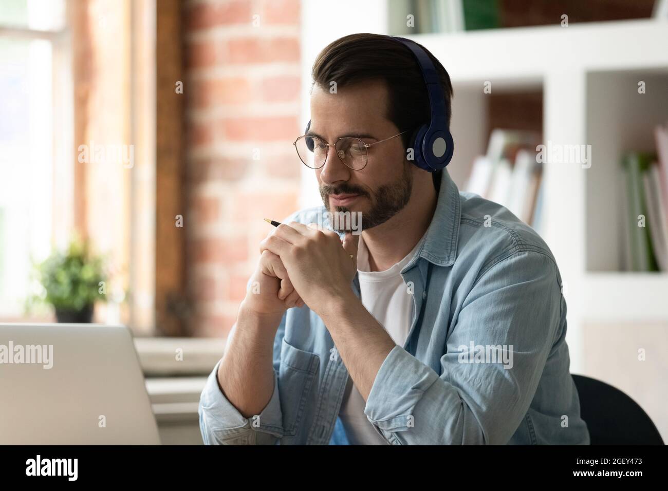 Un homme attentif utilise un ordinateur portable pour écouter le cours audio à l'aide d'un casque Banque D'Images