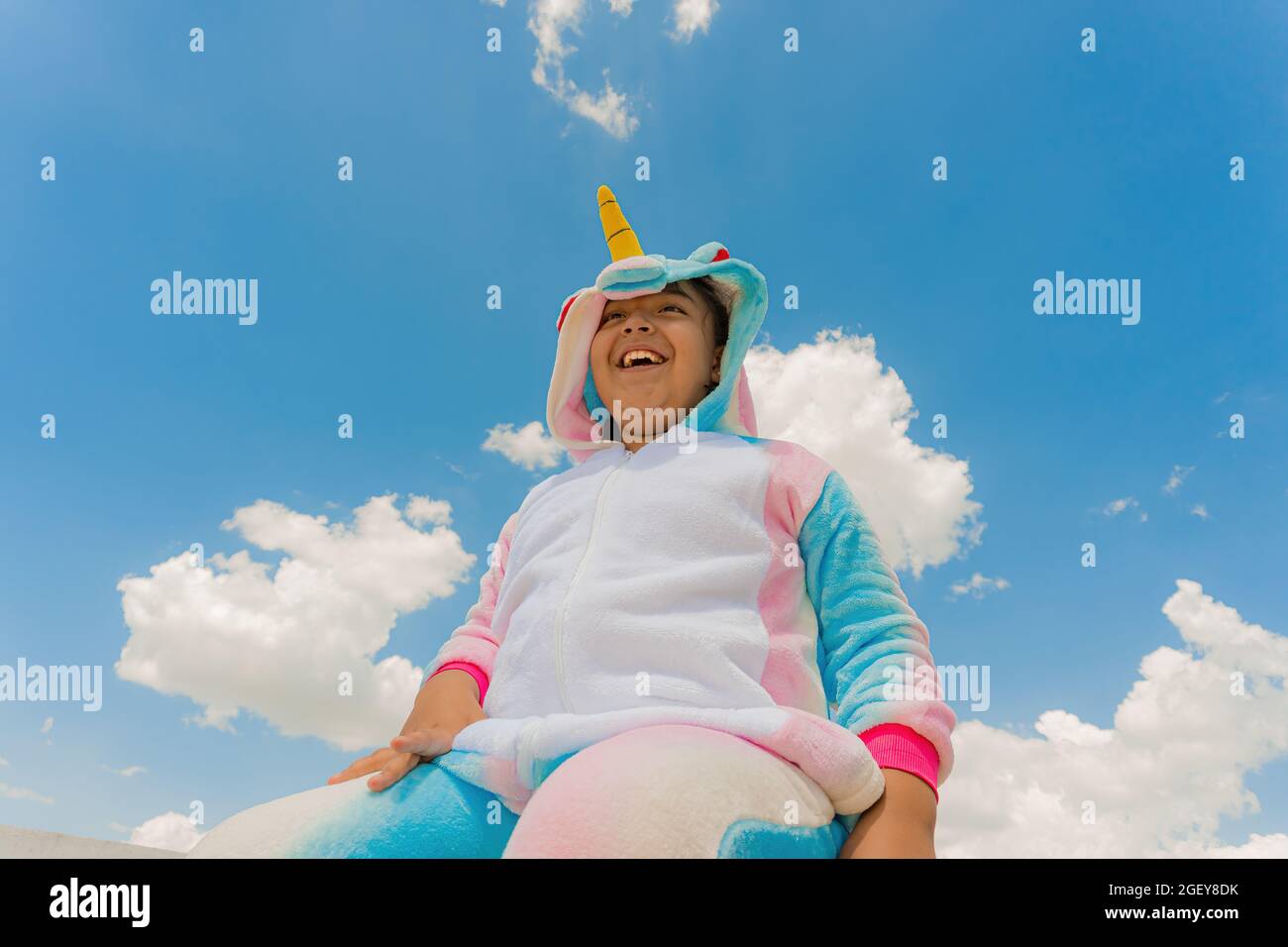 Gros plan d'un joyeux garçon hispanique en costume de licorne et ciel bleu sur le fond Banque D'Images