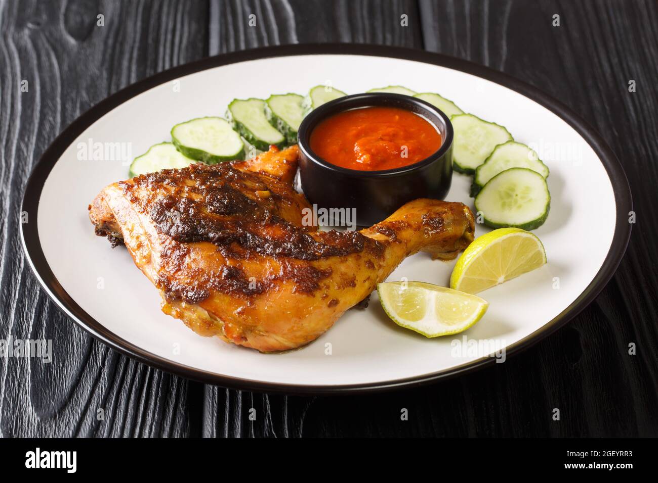 Savoureux poulet grillé Ayam Bakar chaud servi avec concombre, citron vert et sauce dans l'assiette sur la table. Horizontale Banque D'Images