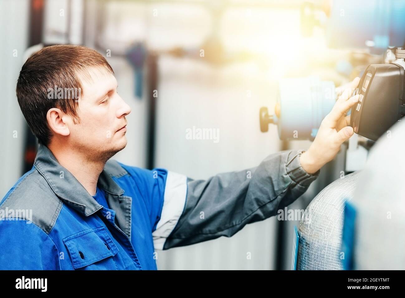 Le technicien en électricité vérifie le système et les relevés dans l'installation de production intérieure. Il s'agit d'un vrai travailleur caucasien en combinaison pendant qu'il travaille Banque D'Images