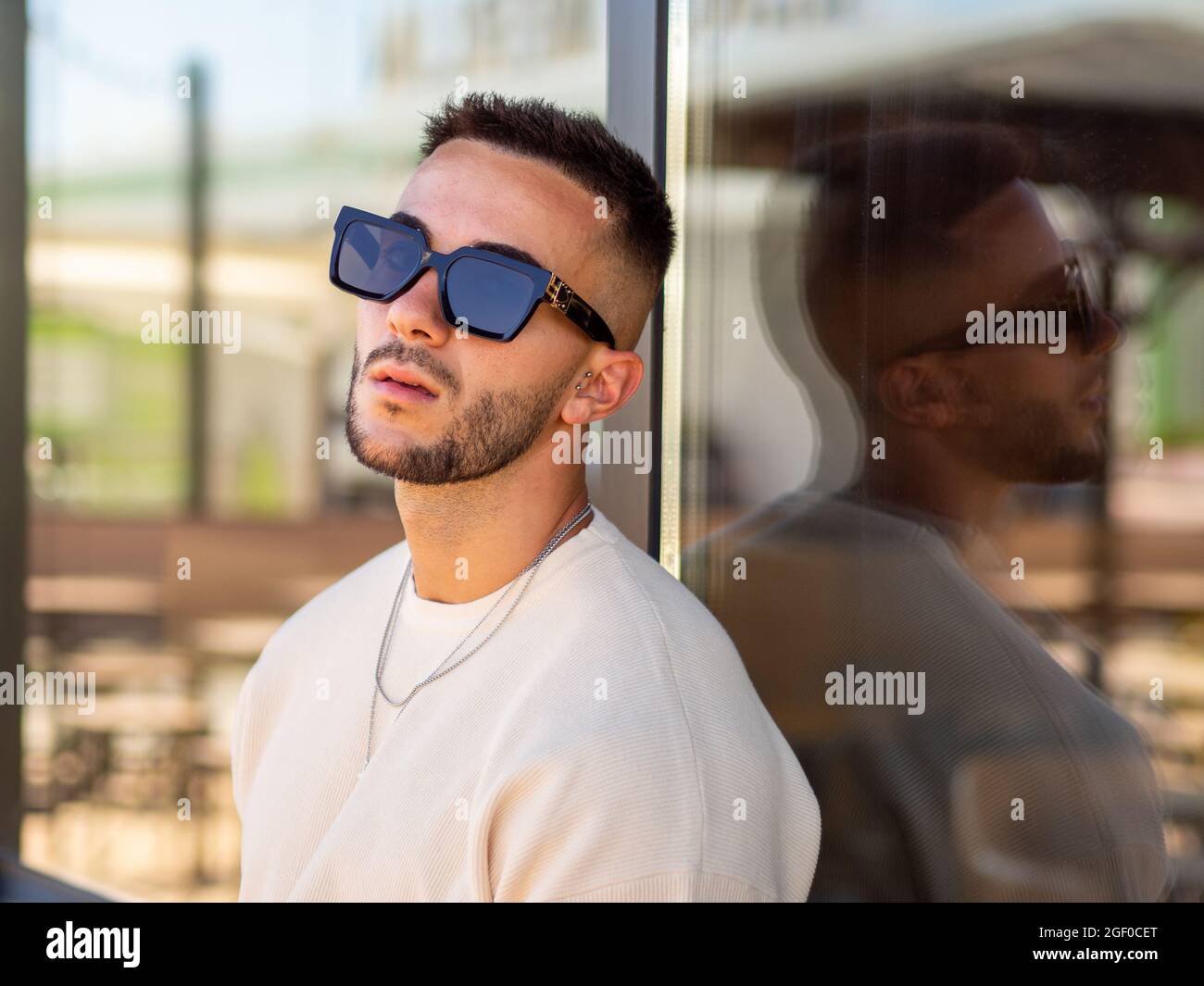 Un portrait d'un homme espagnol frais avec des lunettes de soleil penchées  sur un mur de verre d'un bâtiment Photo Stock - Alamy
