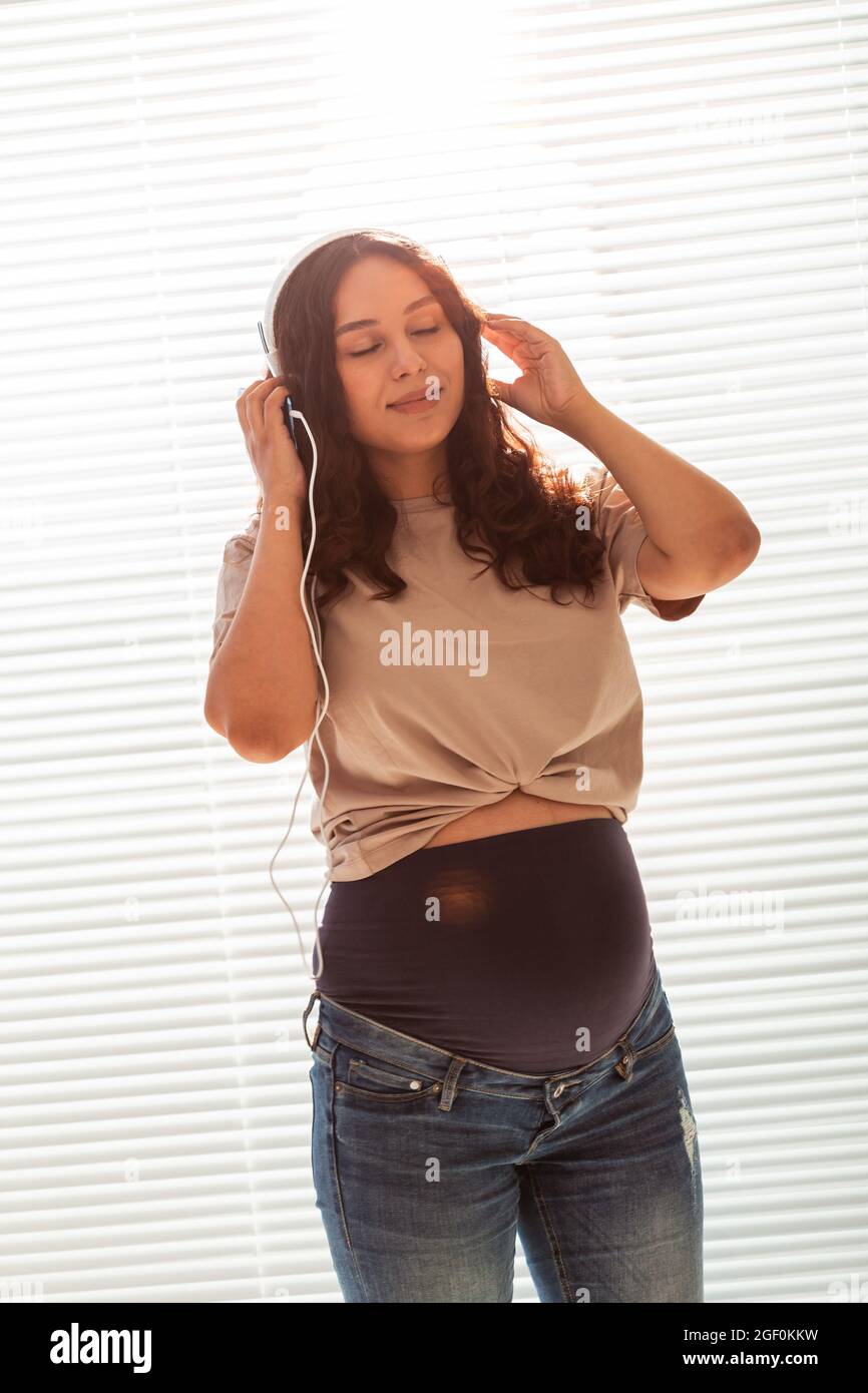 La femme enceinte écoute de la musique dans un casque à la maison et danse Banque D'Images