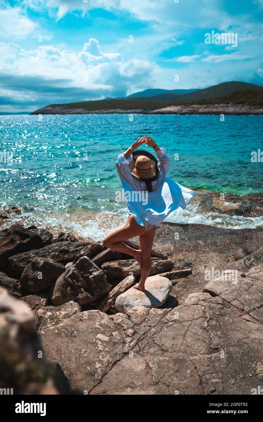 Belle femme vue de derrière debout sur une plage de pierre sur la rive de l'île de vis en Croatie. Agitant ses bras de manière hapeuse en posant, debout sur un Banque D'Images