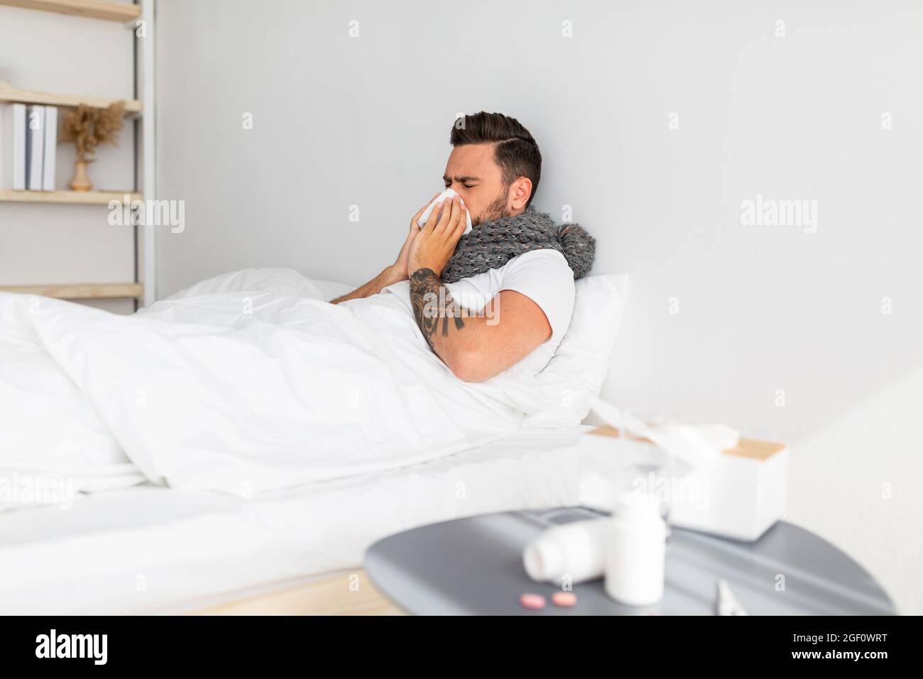 Traitement à domicile contre le rhume, la grippe et la covid-19. Malade jeune gars soufflant le nez dans la serviette, allongé dans le lit Banque D'Images