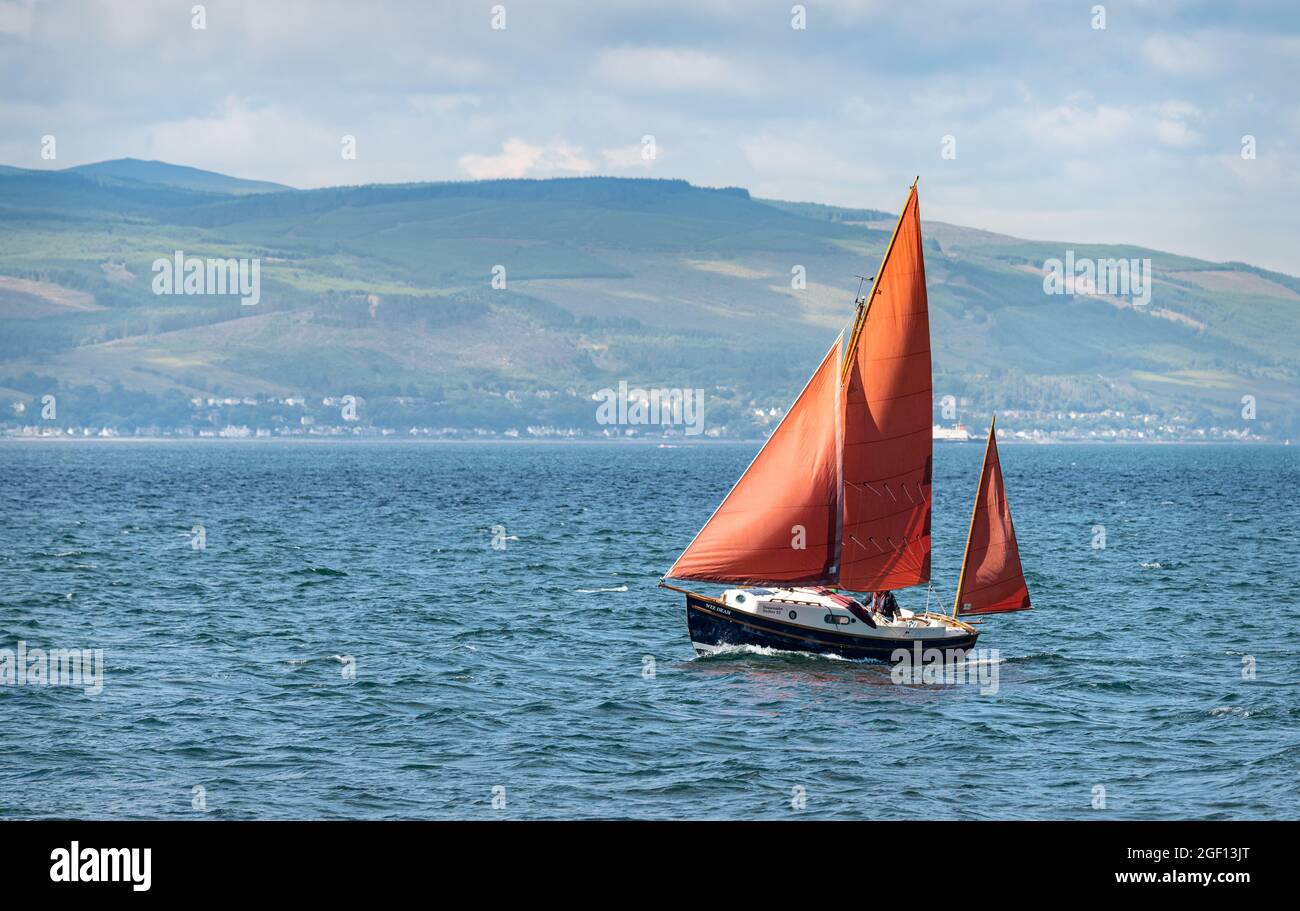 Bateau à voile, Wee DRAM, avec voiles rouges dans le firth de Clyde avec l'île de Bute en arrière-plan, Cumbrae, Écosse Banque D'Images