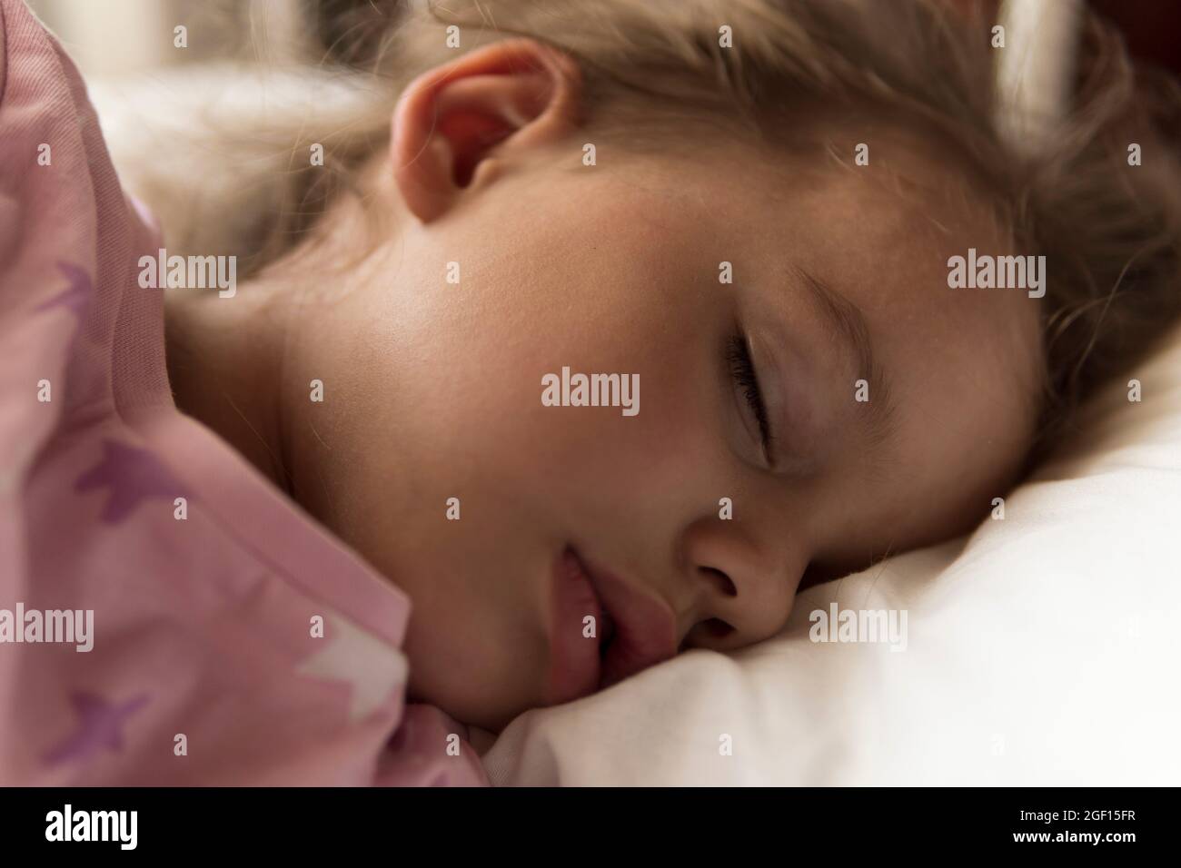 Mignon gai petit 3-4 ans préscolaire bébé fille enfant dormir doux dans un lit de bébé blanc pendant le déjeuner temps de repos dans un pyjama rose avec un oreiller à la maison Banque D'Images