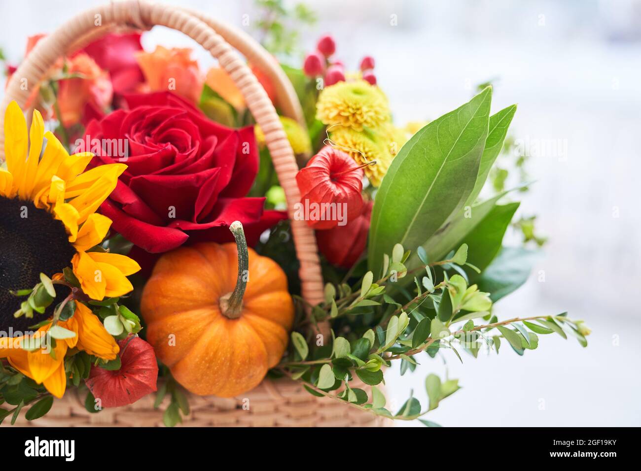 Gros plan d'un panier avec de belles fleurs d'automne faites de roses rouges, de tournesol et de feuilles vertes. Le concept des vacances. Espace de copie photo de haute qualité Banque D'Images