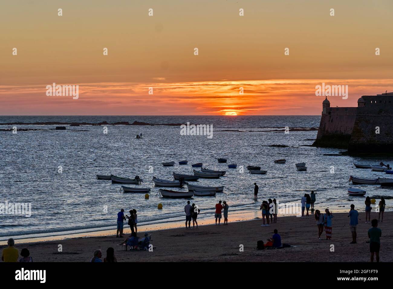 Image rétro-éclairée d'une plage à Cadix (Espagne) au coucher du soleil, montrant les gens et les bateaux amarrés après la pêche, lors d'une belle journée d'été. Banque D'Images