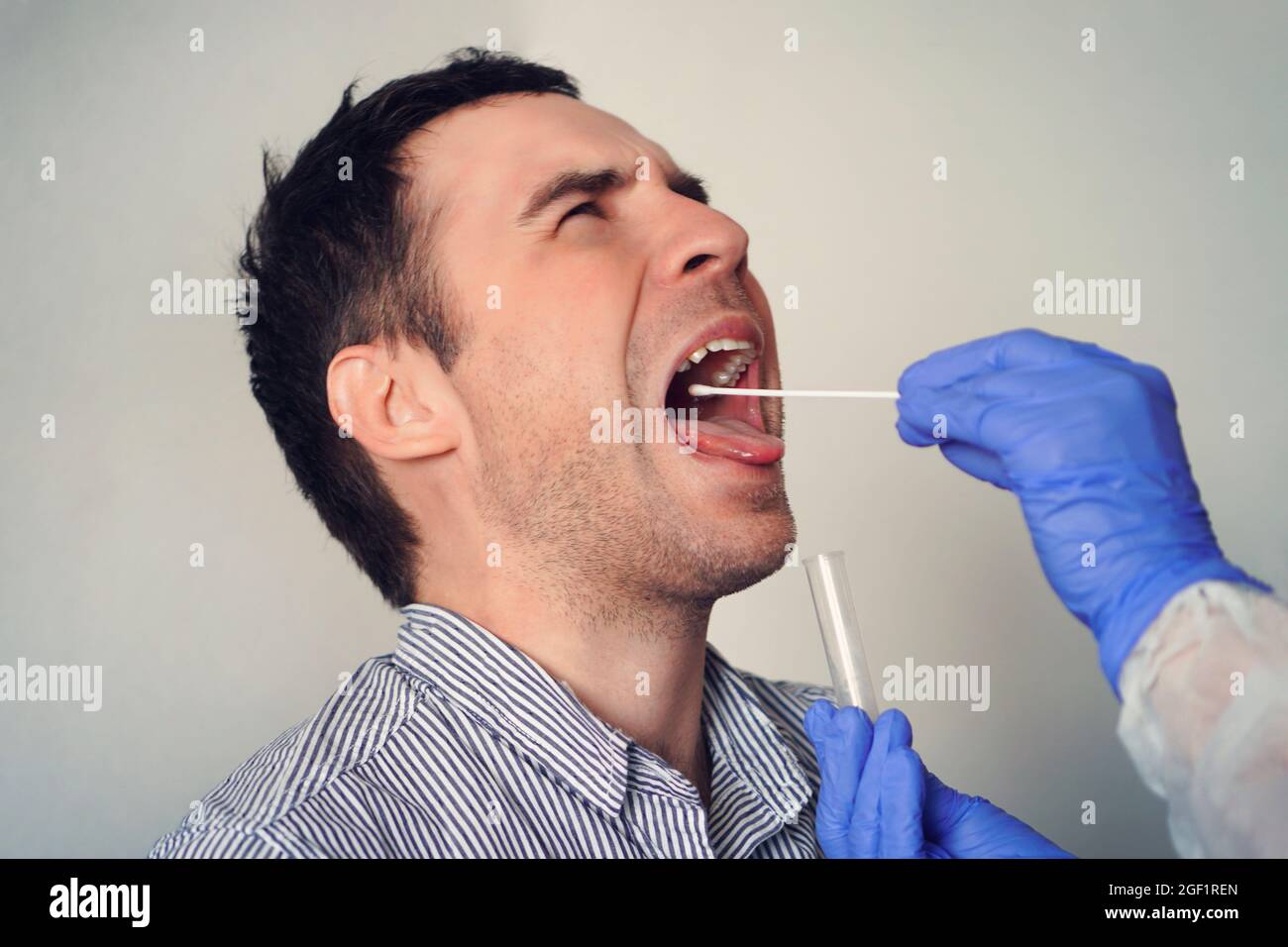 Médecin effectuant un test de coronavirus pour un patient mâle. Prélèvement d'un échantillon de salive d'un homme. Test d'ADN. Collection de mucus de la gorge pour la recherche dans le l Banque D'Images