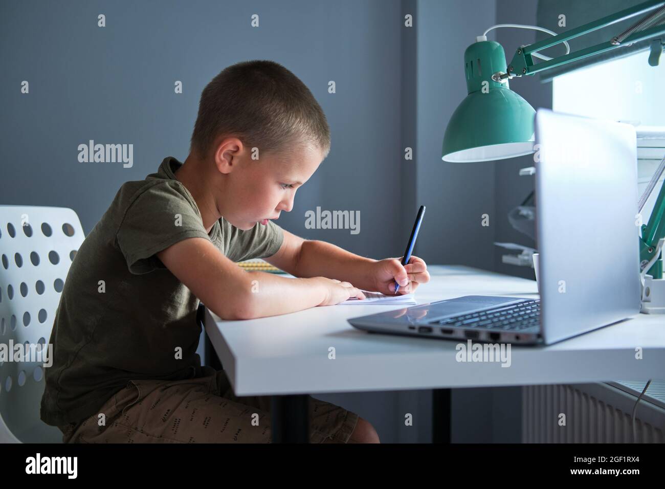 L'élève assis à la table et utilisant un ordinateur portable tout en faisant du travail scolaire à la maison. Concept de homeschooling. Banque D'Images