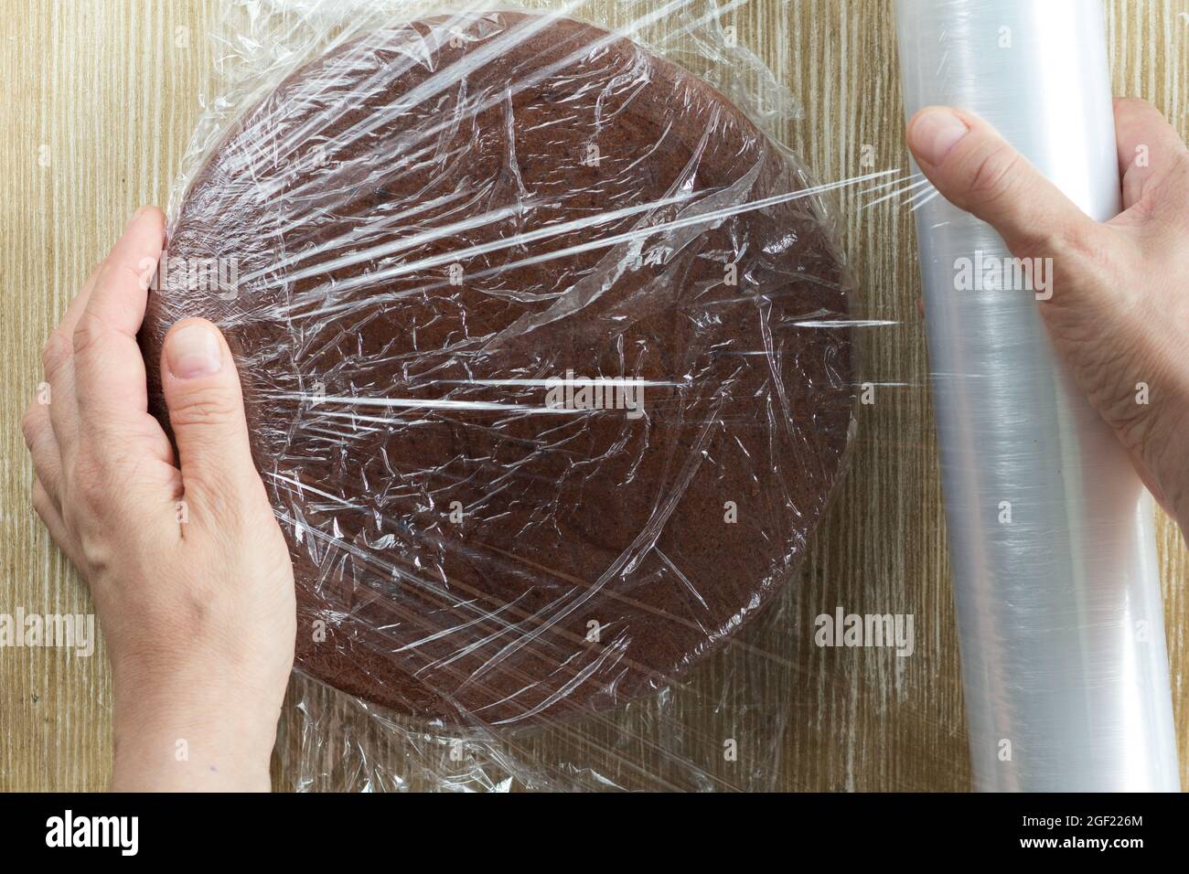 Vue de dessus de la femme emballage main gâteau éponge chocolat en plastique pour le stockage sur fond en bois Banque D'Images