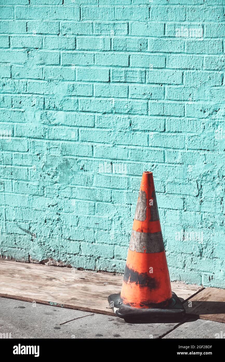 Vieux cône de trafic sale par un mur de brique, foyer sélectif, couleur de virage appliquée. Banque D'Images